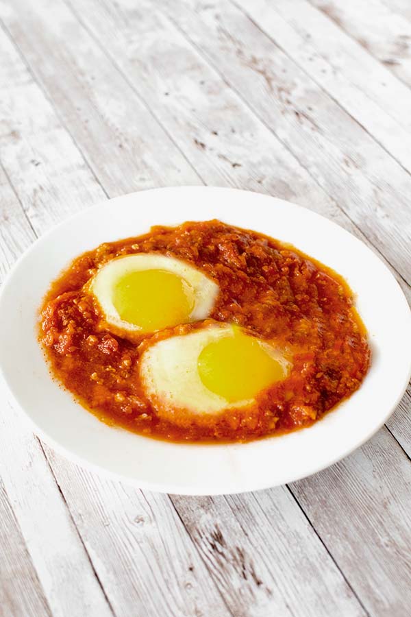 Two eggs in tomato on a white plate