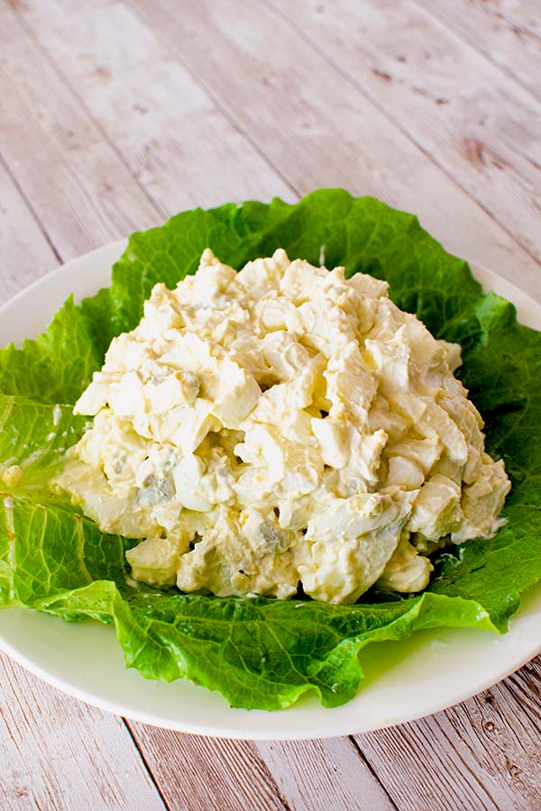 A mound of egg salad on a green leaf of lettuce on a white plate