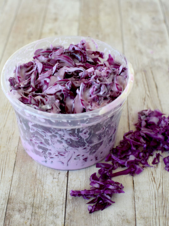 Red Cabbage Salad in a clear deli container on a white wood table