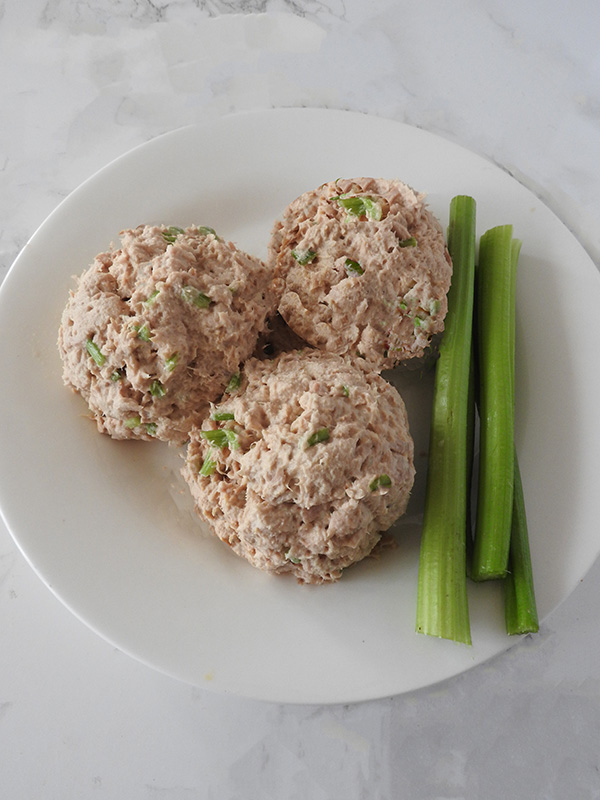 Three balls of tuna with celery and three celery sticks on a round white plate on a white background