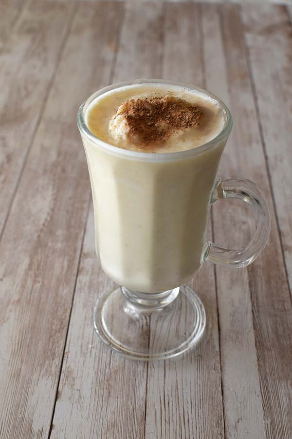 Eggnog in a cappuccino glass on a white plankk board packground