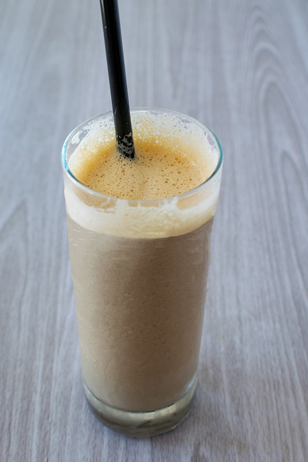 coffee smoothie in a clear glass with a black straw on a white wood background