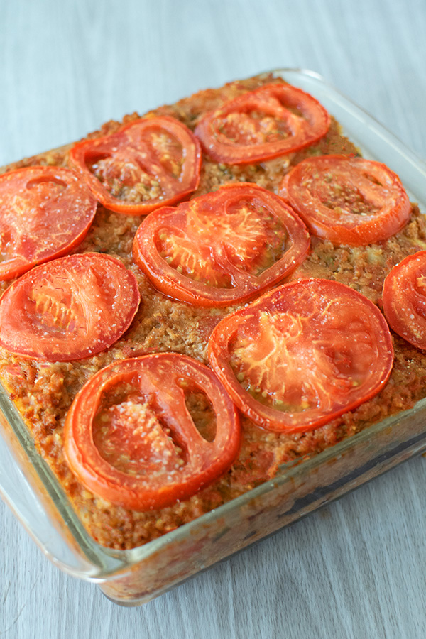 Moussaka for Passover ground beef covered with tomato slices in a clear square baking dish