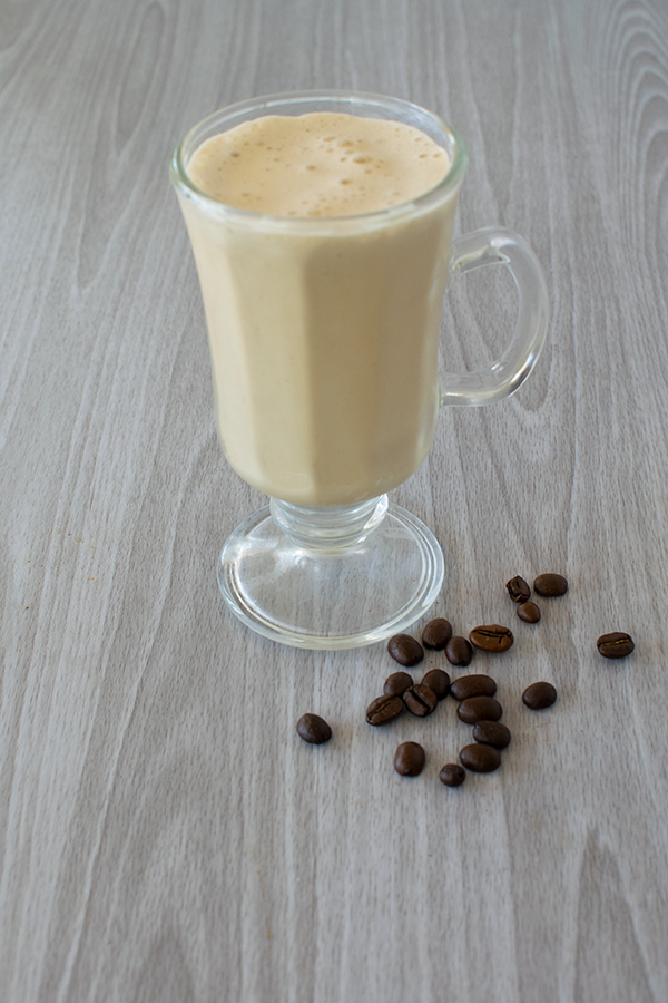 Easy ice smoothie in a cappuccino glass with coffee beans nearby on a white wood background