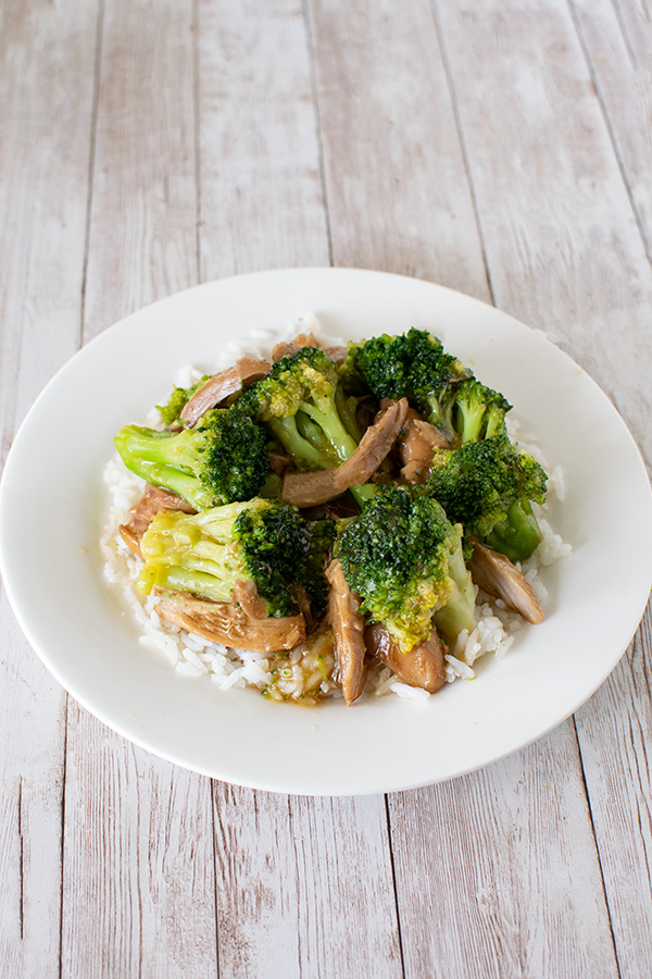 chicken and broccoli over rice on a white plate on a white wood background