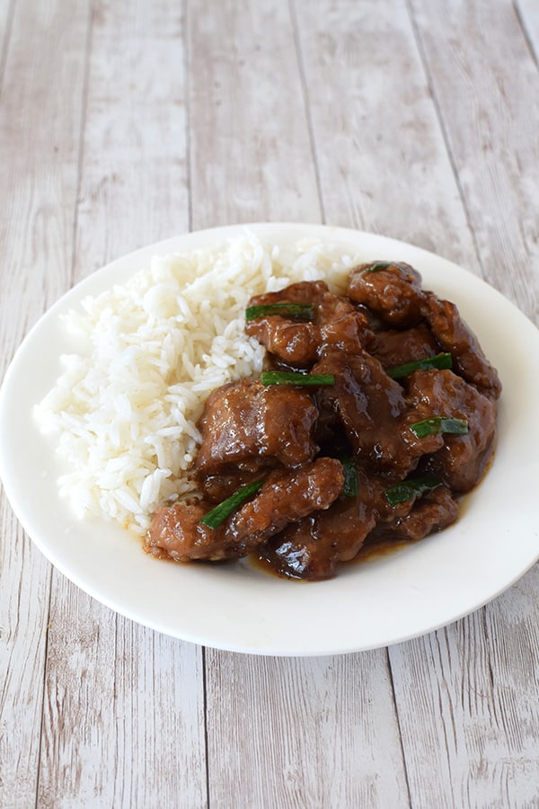 Mongolian Beef with white rice on a white plate on a white wood background