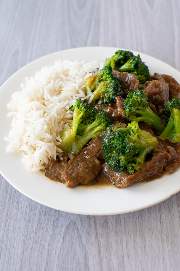 Beef and Broccoli on white rice on a white plate on a white wood background