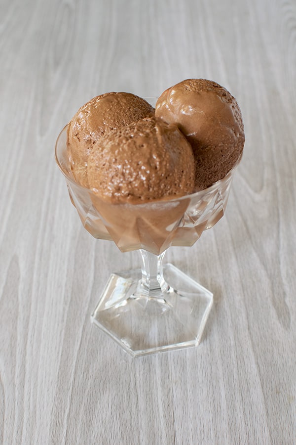scoops of dairy free chocolate ice cream in a clear dessert dish on a white wood background