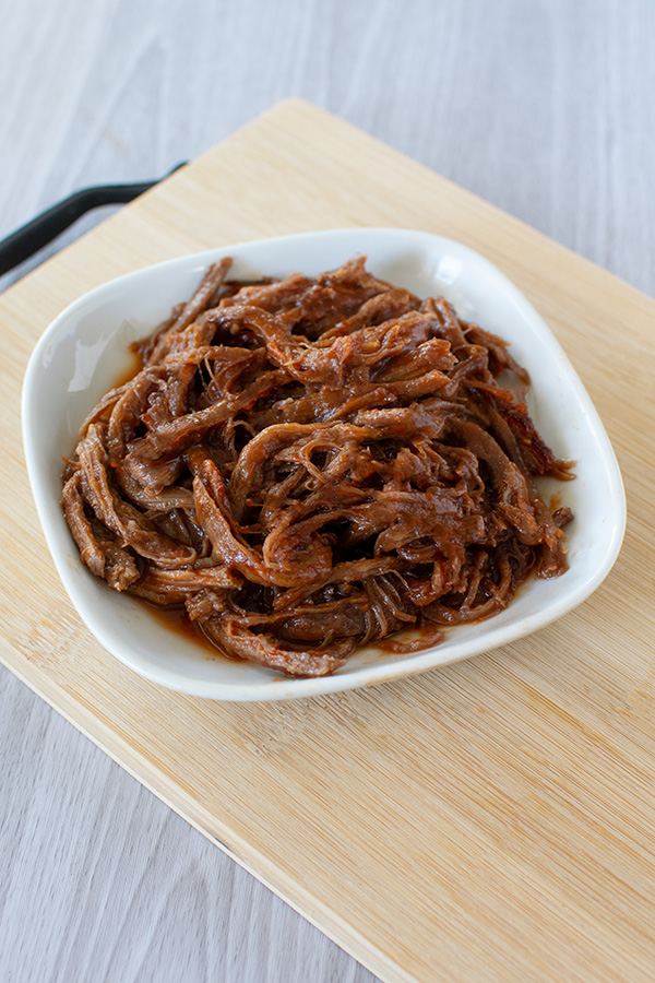 Pulled beef on a square white plate on a wooden cutting board on a white wood background