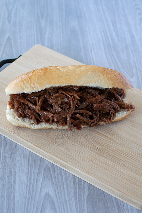 Whole pulled beef brisket on wooden cutting board on a white wood background