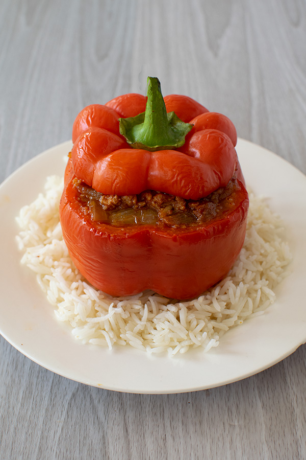 Stuffed pepper with top on white rice on a white plate on a white wood background