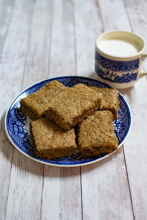 Easy Dairy Free Blondies on a blue plate with a cup of milk nearby on a white wood background