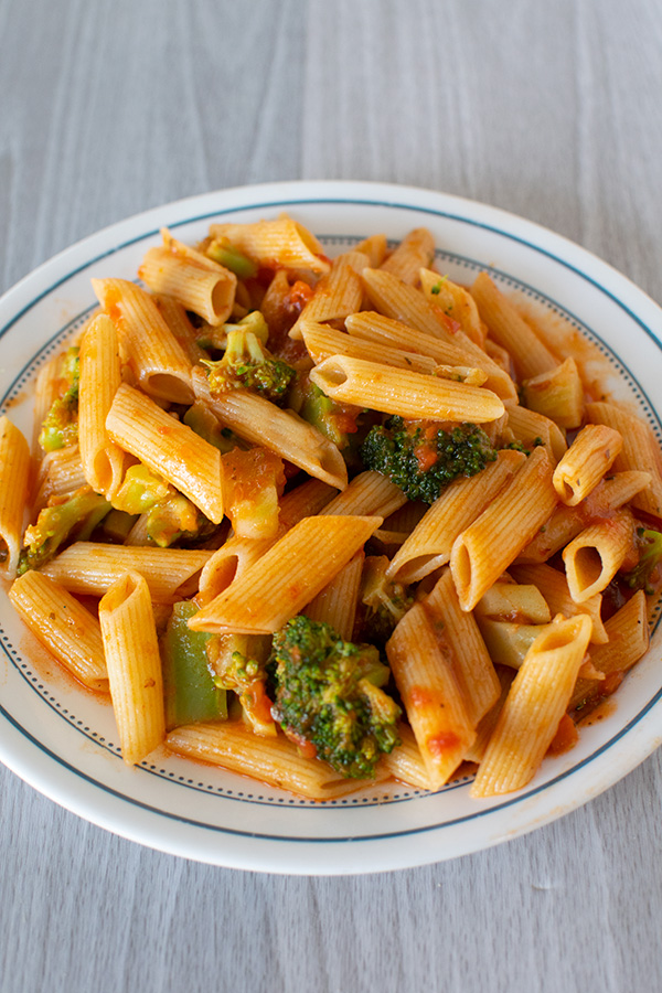 Pasta with sauce and broccoli on a white plate with a blue rim on a white wood background