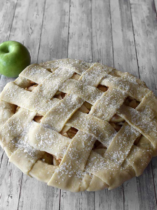 Raw apple pie with a green apple on a white wood background