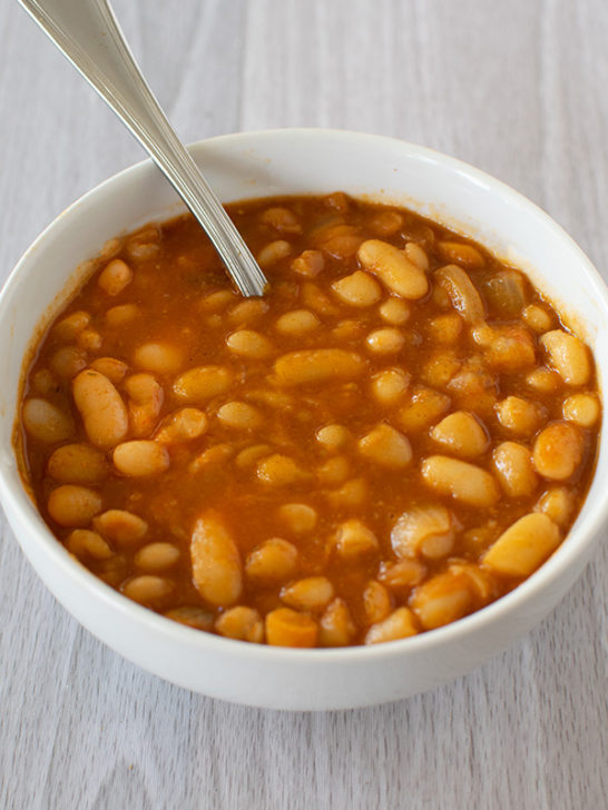 Israeli bean soup in a white bowl with a spoon and all on a white wood background