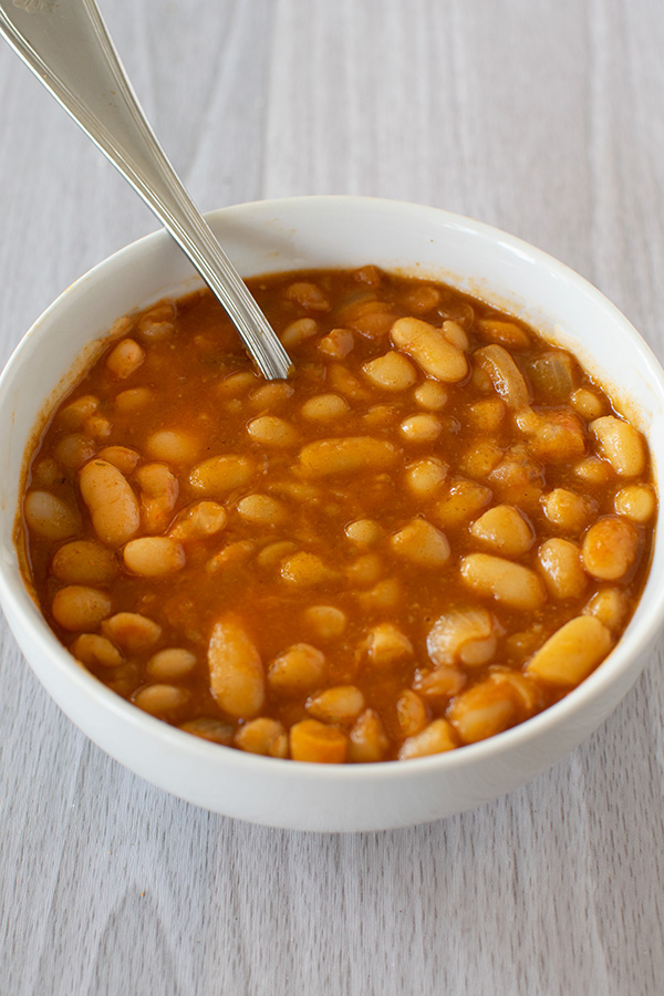 Israeli bean soup in a white bowl with a spoon and all on a white wood background