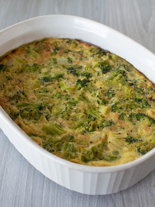 Easy Broccoli kugel in a white deep oval serving dish on a white wood background