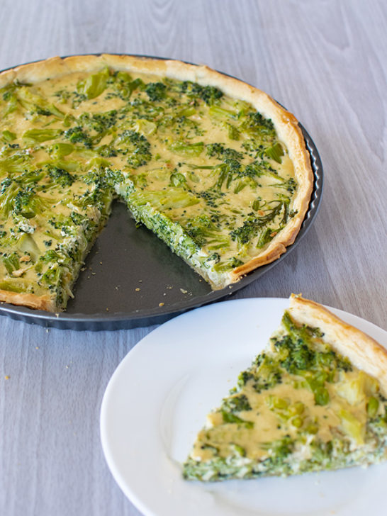 Broccoli quiche without cheese in a tort pan with a slice removed, but on a white plate - all on a white wood background