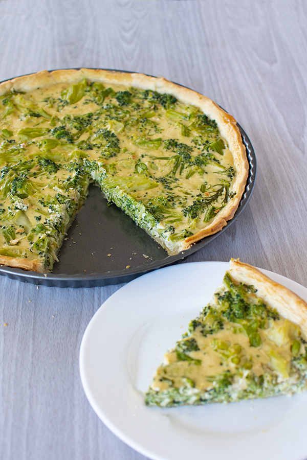 Broccoli quiche without cheese in a tort pan with a slice removed, but on a white plate - all on a white wood background