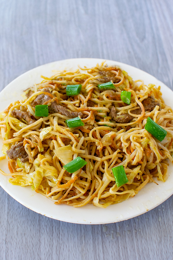 Beef Chow Mein topped with pieces of green onion on a white plate on a white table