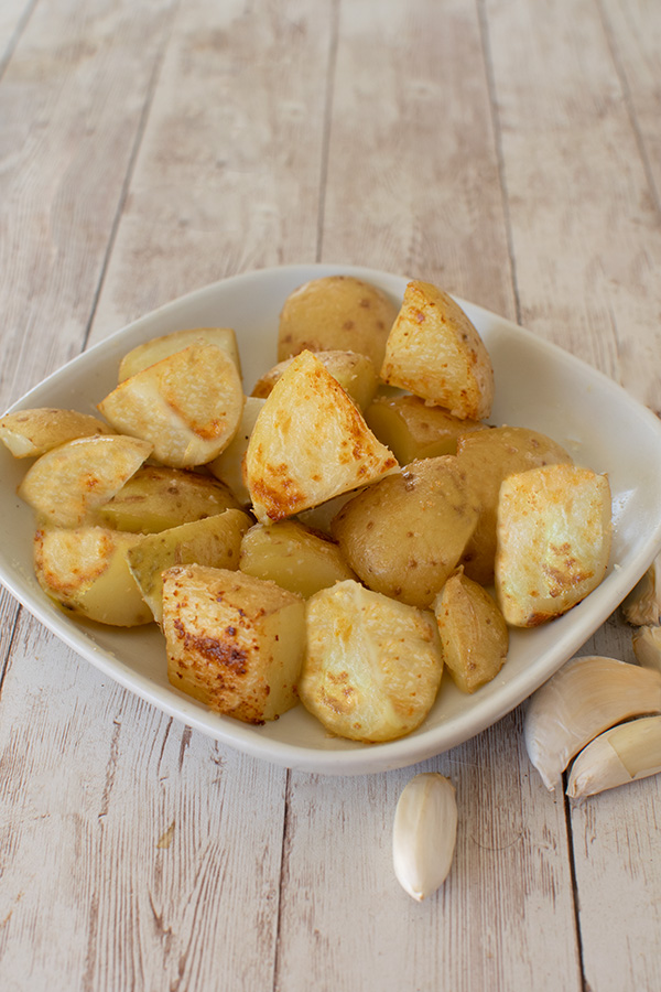 Vegetarian Roasted Garlic potatoes on a square white plate on a white table with garlic cloves nearby