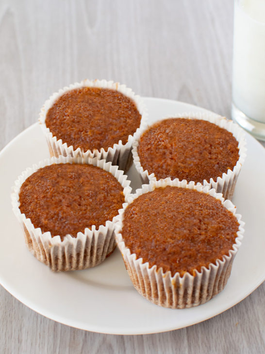 4 Dairy free honey muffins on a white plate with a clear glass of milk on a white table