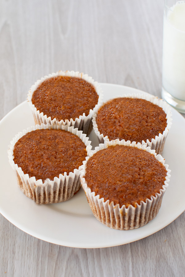 4 Dairy free honey muffins on a white plate with a clear glass of milk on a white table