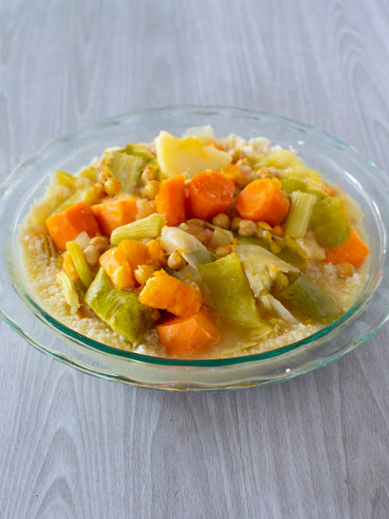 Israeli Vegetable soup on couscous in a clear bowl on a white wood table