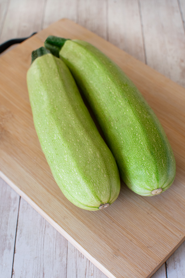 Two light green zucchinis on a bread board
