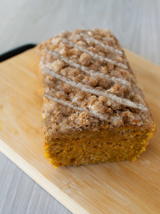 Pumpkin Loaf Cake with streusel and icing sliced open on a bread board on a white wood table
