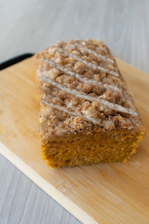 pumpkin cake loaf with streusel and icing sliced open on a bread board on a white wood table