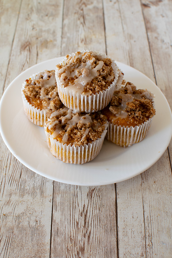 A pile of Pumpkin muffins with streusel on a white plate on a white wood table