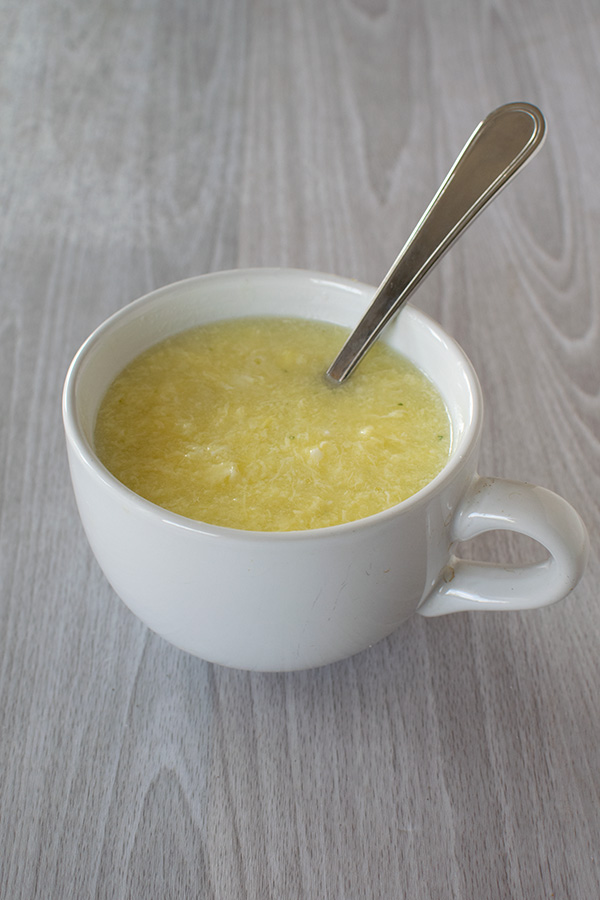 Egg drop soup in a white soup mug with a spoon on a white wood table