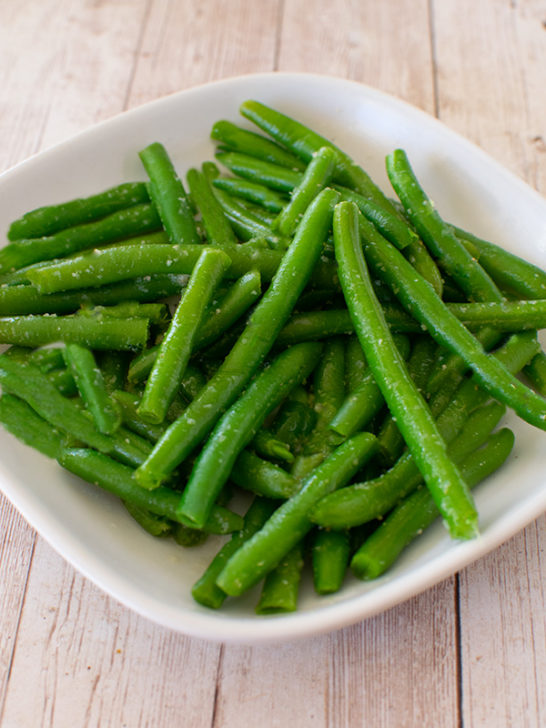 Garlic Green beans on a white square plate on a white wood table