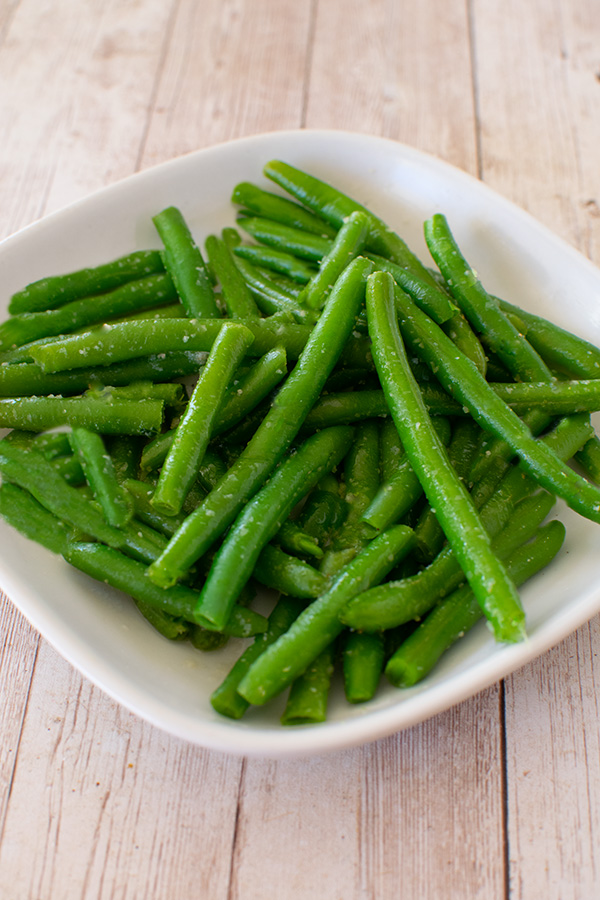 Garlic Green beans on a white square plate on a white wood table