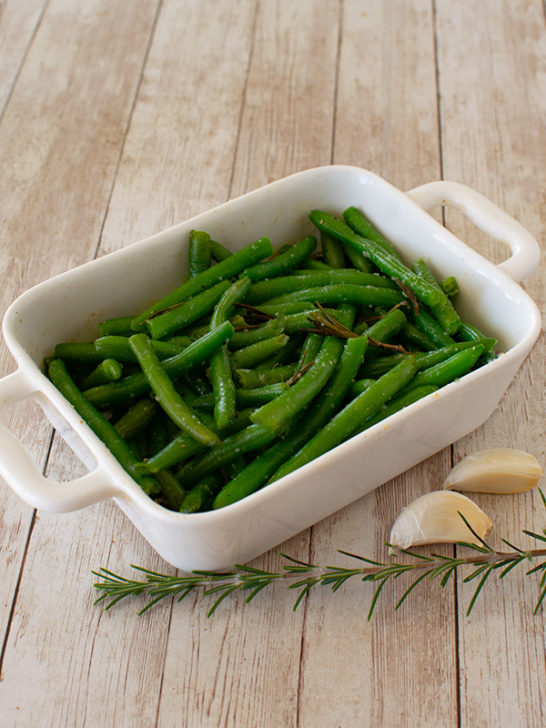 Garlic and Rosemary Green beans in a white rectangular baking dish on a white wood table
