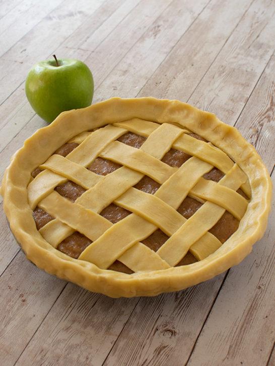Raw mock apple pie with a green apple nearby on a white board table