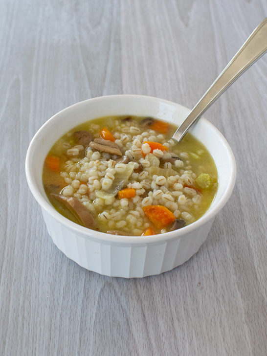 Vegetarian Mushroom Barley Soup in a white bowl with a spoon on a white wood background