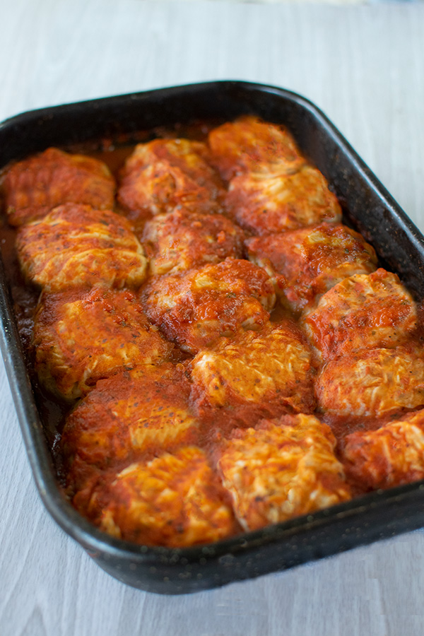 5 rows of stuffed cabbage on a black pan on a white wood table