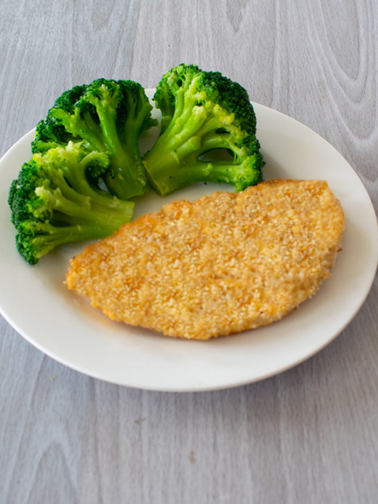Fish Schnitzels on a white plate with broccoli on a white wood table