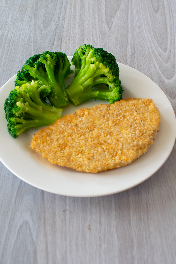 Fish Schnitzels on a white plate with broccoli on a white wood table