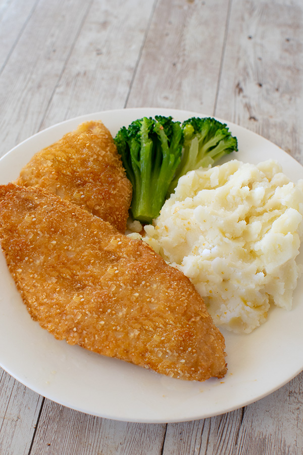 2 pieces of Fried potato flake fish on a white plate with mashed potatoes and broccoli