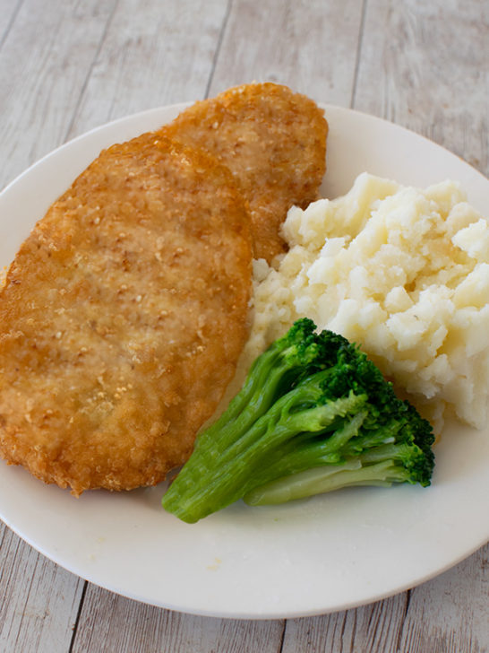 Two Potato Flake Schnitzels on a white plate with broccoli and mashed potatoes on a white wood background
