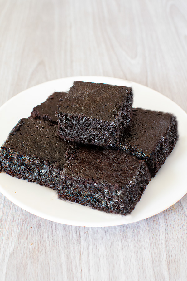 Several Dairy Free Chewy Brownies on a white plate on a white wood background