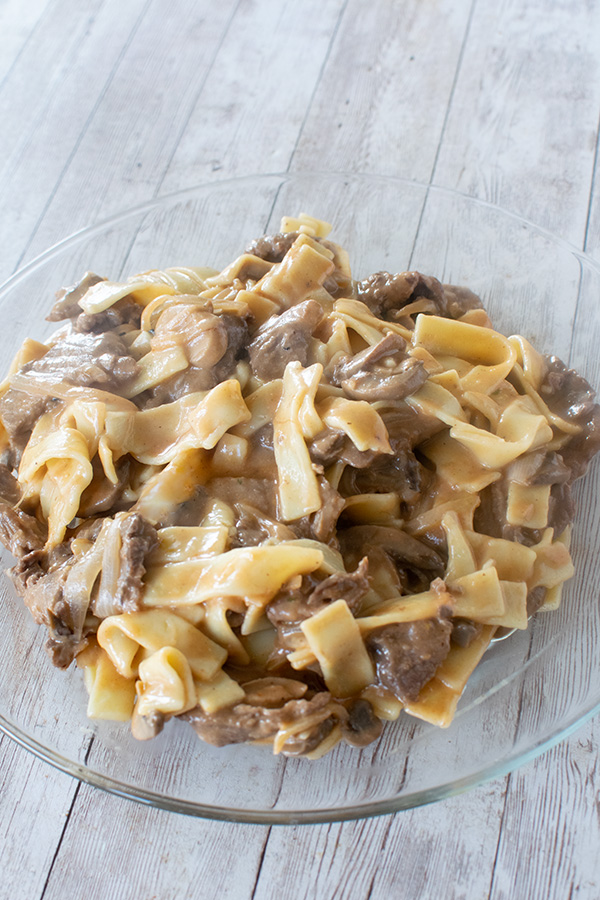 Creamy dairy free beef stroganoff made with  long flat noodles served on a clear plate.