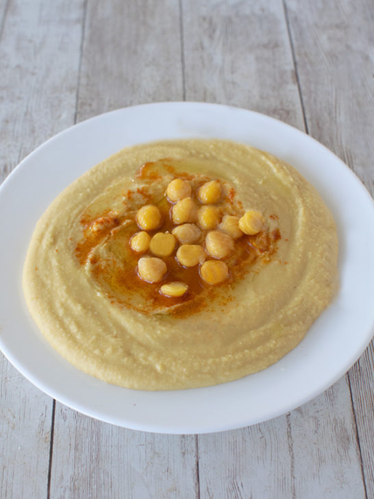 White plate with hummus and olive oil in the middle with chickpeas and paprika