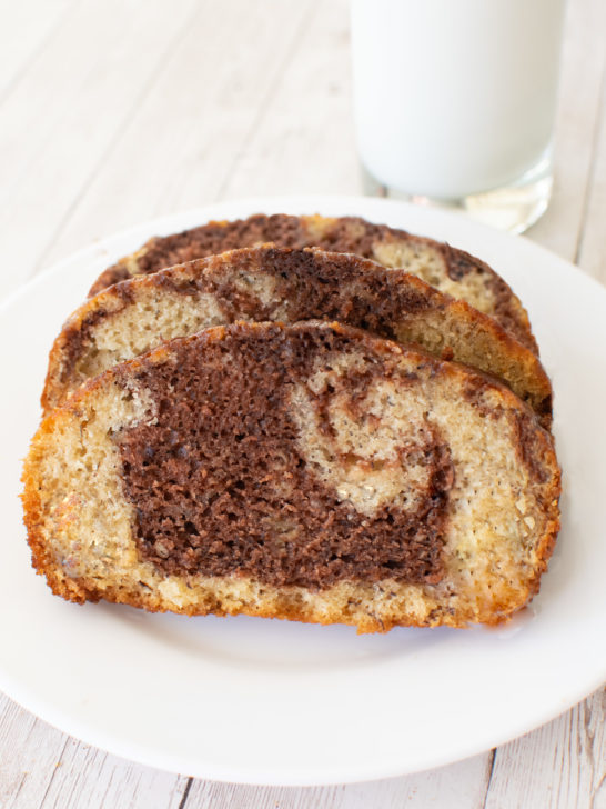 Slices of Easy Chocolate Banana Marble Cake on a white plate near a glass of milk on a white wood table