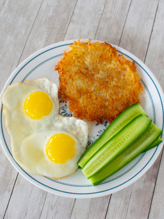 Easy hash browns on a plate with two sunnyside up eggs and sliced cucumber