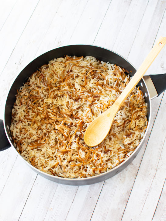 Easy Rice Vermicelli in a pan with black handles and a wooden spoon inside on a white wood table.