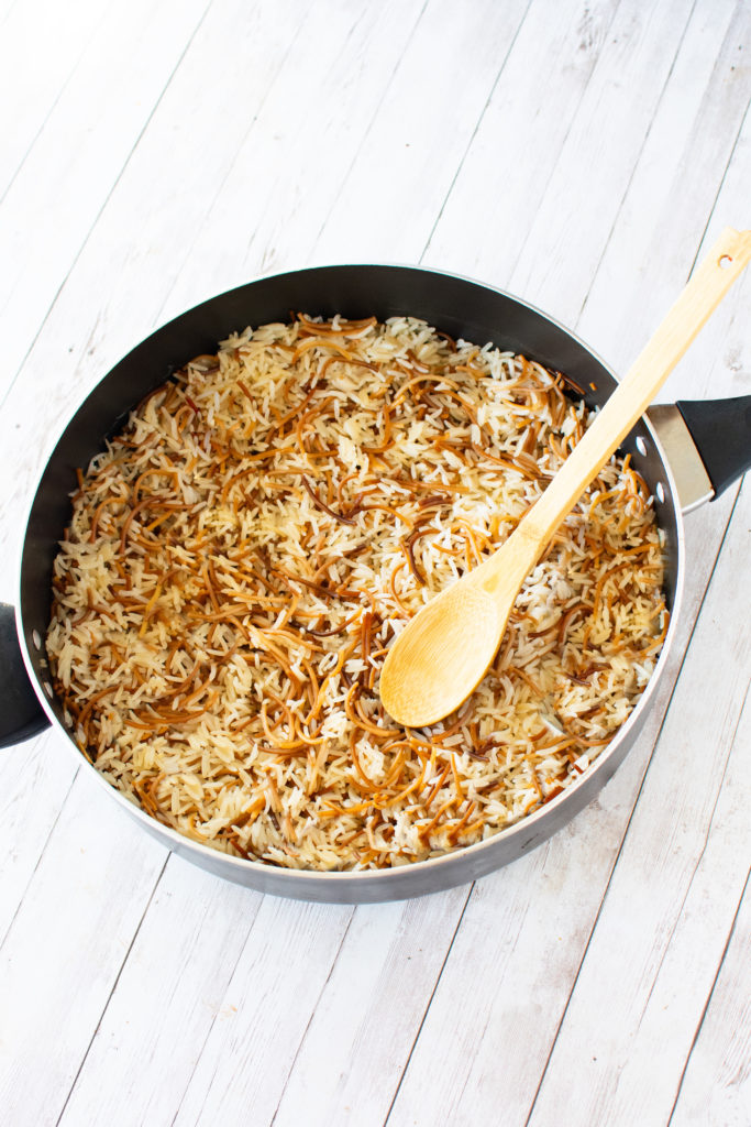 Easy Rice Vermicelli in a pan with black handles and a wooden spoon inside on a white wood table.